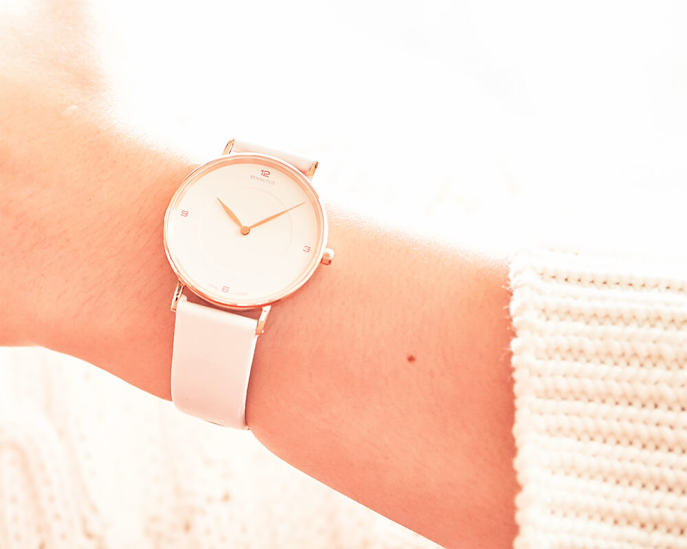 シンプルな白文字盤にピンクのインデックスに白いスムーズレザーの腕時計をしている女性